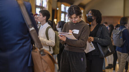 A student stands in line at the UMSI career fair, holding a folder and making notes with a pencil.
