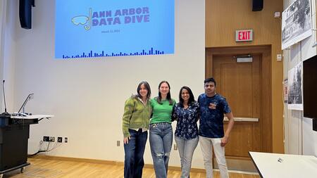 Four students standing together under a projected sign that says "Ann Arbor Data Dive"