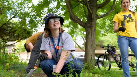 A UMSI student holds a shovel and smiles while working in a rain garden 