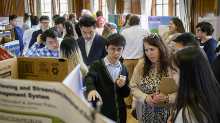 Students show a UMSI board member their poster at the 2023 UMSI Student Project Exposition