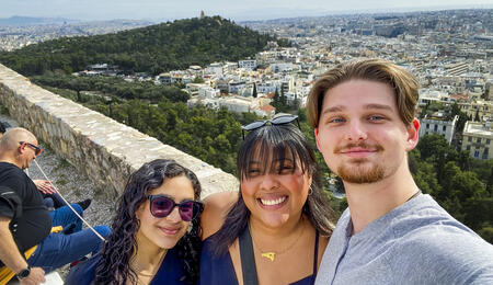 Three people taking a selfie overlooking a forest and a city