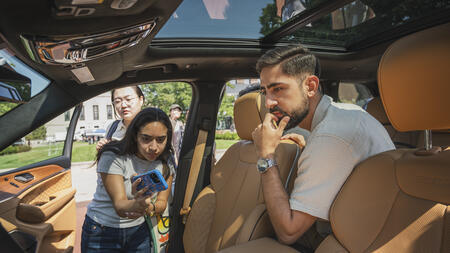An interior view of a vehicle as three UMSI students study the user interface, with one taking a photo on their cell phone