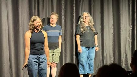 Gabriela Marcu gestures on stage with two other people beside her