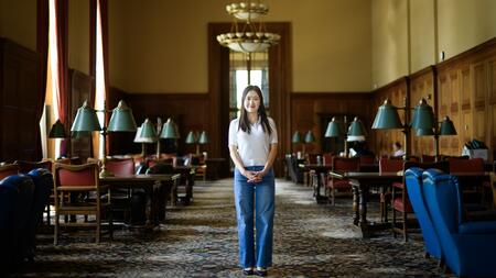 Jane Im stands in a carpeted room in Rackham with dark wood tables lining either side
