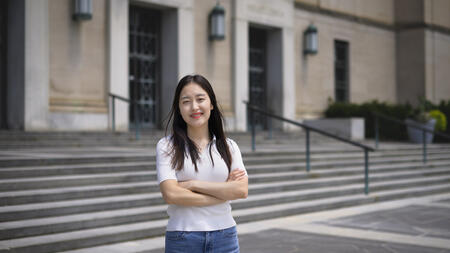 Jane Im stands in front of an academic building, arms crossed in front of her 