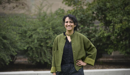 Amina Abdu smiles into the camera while standing outside wearing a green cardigan.