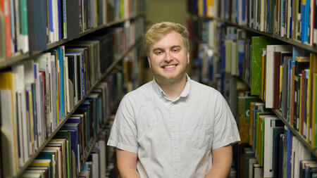 Austin Book poses in the library stacks with books on either side of him