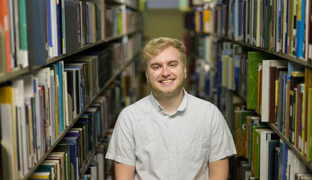Austin Book poses in the library stacks with books on either side of him