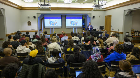 Ben Marchionna stands in front of a presentation screen speaking with a crowded room