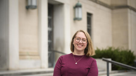 Rebecca Frank wearing a maroon sweater, a neckplace and glasses and smiling at the camera. 