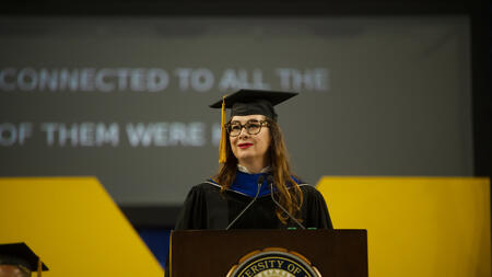 Marta Rey Babarro stands at a podium with the top of a large Block M and a screen visible behind her 