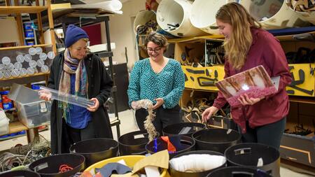 Three people sorting craft supplies in a room full of buckets.