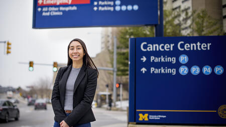A student standing next to a sign that says "Cancer Center parking."