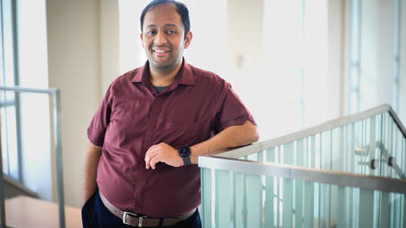Venkatesh Potluri poses with one arm resting on a metal and glass railing inside a building