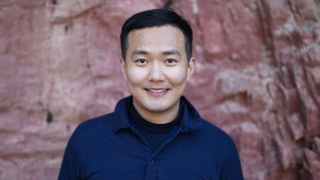 A person smiling with short dark hair wearing a black shirt. 