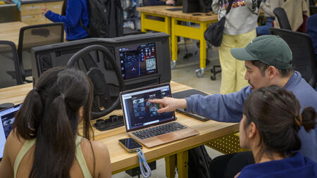 Three people face a computer screen and car dashboard prototype, as one collaboratively points to an element on-screen