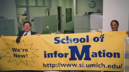 Daniel Atkins and Olivia Frost hold a bright yellow banner that reads "School of Information" and "We're new!"