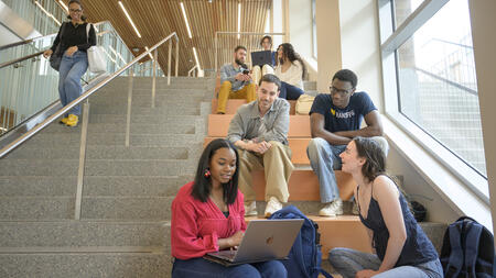 Masters students sit and talk on a main lobby stairwell in the Leinweber building.