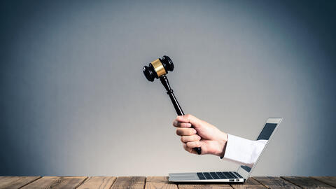 A hand holding a gavel coming out of a laptop screen