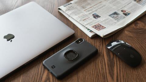 a laptop, a smartphone, a wireless mouse, and a newspaper arranged on a table