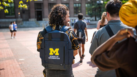 A UMSI student on the U-M Ann Arbor campus sporting a backpack featuring the UMSI logo.