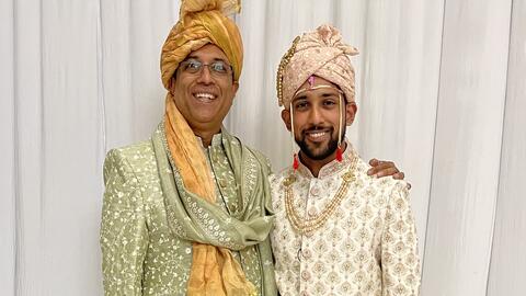 Father and son Nick and Ani Madurkar stand side by side wearing traditional Indian wedding clothing. 