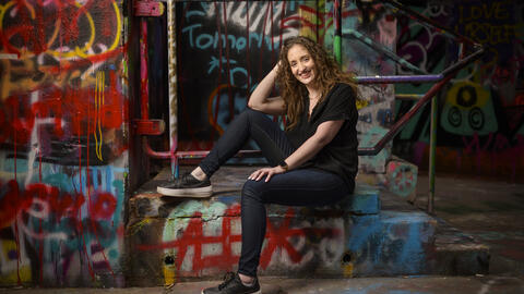 Michaelanne posing in graffiti alley in Ann Arbor, wearing jeans and a black shirt. 