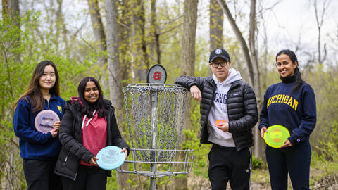 Four people stand in the woods at a disc golf course