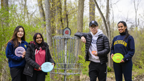 Four people stand in the woods at a disc golf course