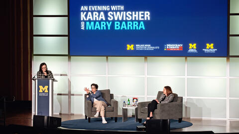 A photo of Kara Swisher and Mary Barra sitting on the stage, with Andrea Forte standing behind a podium