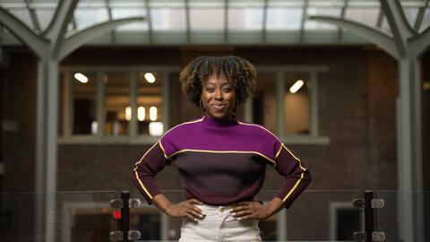 Robin Brewer stands with both her arms at her hips, wearing a sweater and smiling into the camera. 