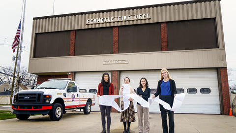 Four students hold a long document in front of a fire station in ferndale