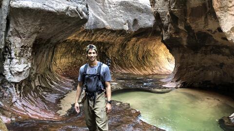 Ermias wears waders and stands in a stream in a rocky canyon