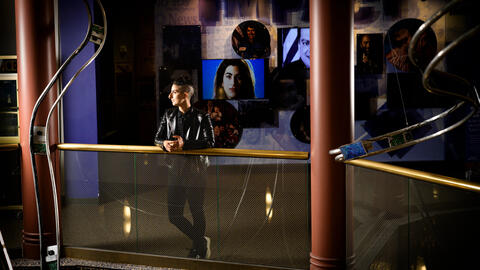 A photo of Tam Rayan posing inside the Arab American National Museum with images projected on a wall behind them