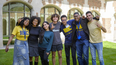 Seven CCSI fellows pose on the grass outside of North Quad, smiling and holding up peace signs