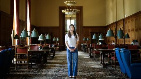 Jane Im stands in a carpeted room in Rackham with dark wood tables lining either side