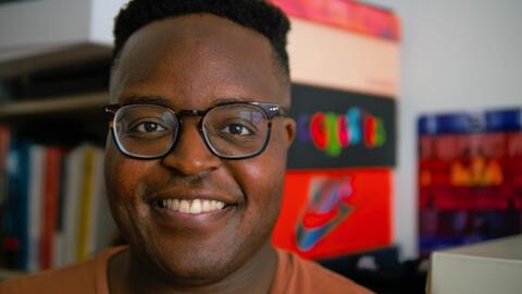 A headshot of Hope Tambala with colorful shelves and file boxes visible behind him
