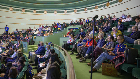 A side view of a packed crowd seated in elevated rows in the seafoam green Rackham Amphitheatre