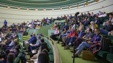 A side view of a packed crowd seated in elevated rows in the seafoam green Rackham Amphitheatre