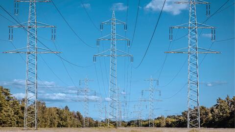 Multiple tall metal electricity transmission towers stretch across an open rural landscape, connected by overhead power lines.