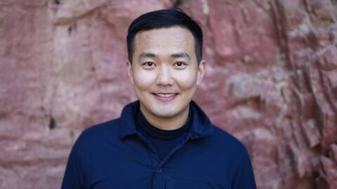 A person smiling with short dark hair wearing a black shirt. 