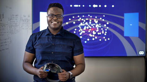 Hope Tambala standing in front of a data visualization holding VR glasses.