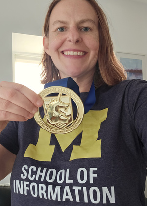 Lydia Schrandt, wearing a UMSI shirt, holds up the medal she earned for completing the 2026 Boston Marathon.