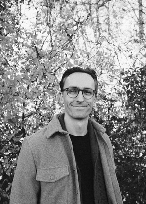A black and white photo of Thomas Seiple standing in front of trees outside.