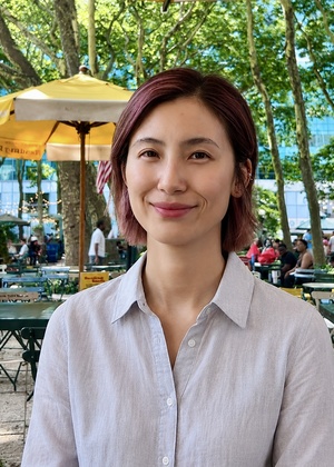 A headshot of Huiran Yi taken outside with trees and tables in the background.