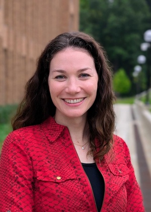 Outdoor photograph of a dark-haired, smiling woman wearing a red shirt