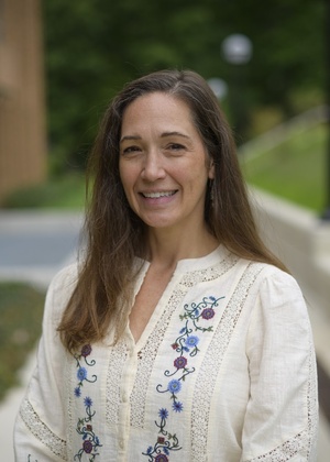 a woman with brown hair in white shirt outside.
