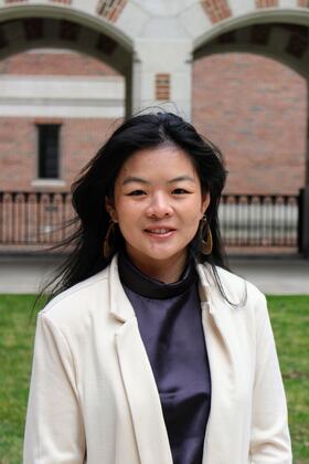 A headshot of Olive Ren in a white blazer in front of the North Quad arches