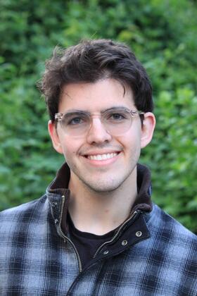 A headshot of Alex Kutsupis in front of a lush green natural background
