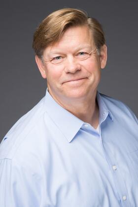 A headshot of John Thompson against a dark gray background